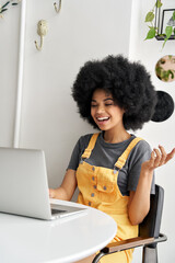 Happy hipster African American woman, young female student with Afro hair talking using laptop...