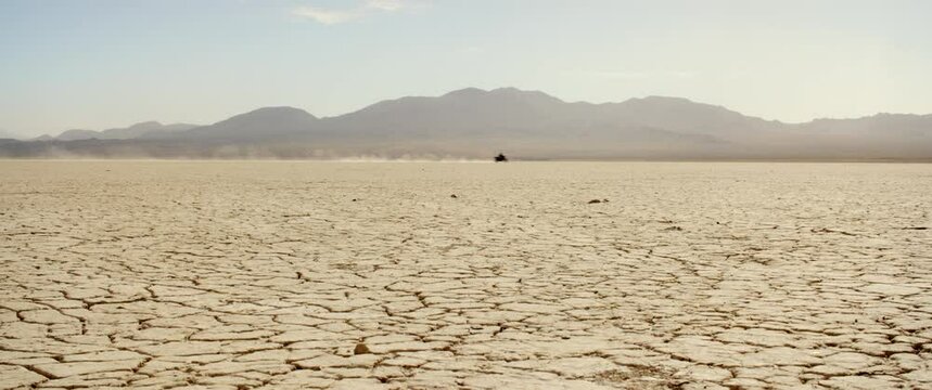 Extreme wide as black motorcycle trails dust across cracked desert