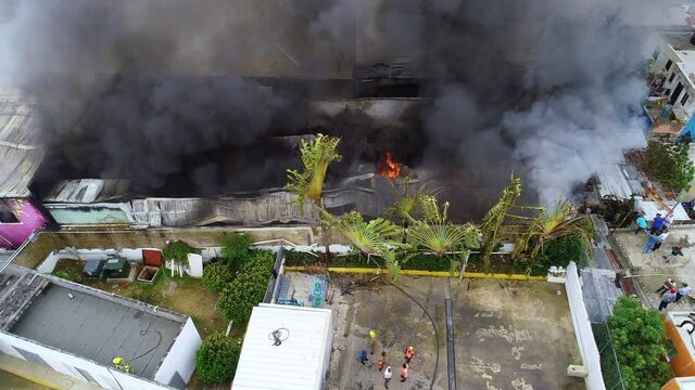 Aerial view overlooking firemen in front of a burning building, dark smoke rising, in Haiti - ,tilt up drone shot