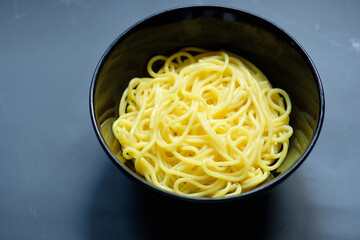 The noodles are in a bowl  placed on table.yellow noodle in black bowl with copy space.