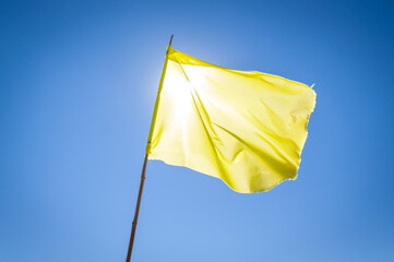 Yellow flag waving in deep blue sky in between the bright sun and the viewer