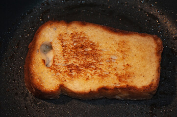 art photo of croutons from a slice of bread fried in butter on a black frying pan