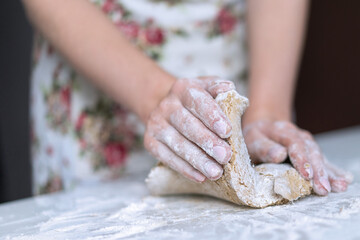 Obraz na płótnie Canvas A young girl kneads dough with her hands on the table
