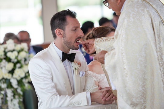 Groom With White Tuxedo Receiving The Communion At Wedding Ceremony