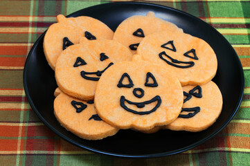 A black plate or orange pumpkin cookies with faces.  Macro, top view.