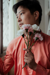 Gay hold a flower looking outside the window.
