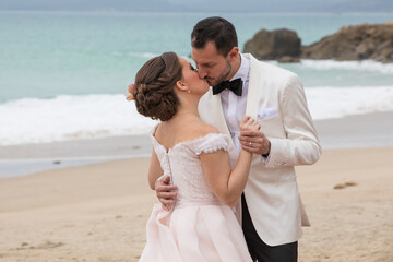 Fototapeta na wymiar Latino Bride and groom with white tuxedo kissing at the beach