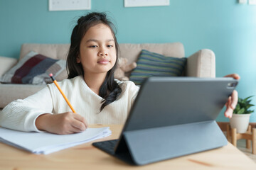  Asian little girl is learning with online tutor on a tablet at home