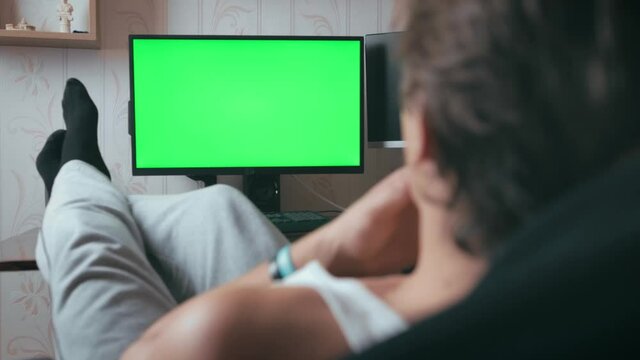 montage of people having fun at home. young guy looks at the green screen. man resting at home. the man has thrown his feet on the table and is watching an advertisement on the monitor.