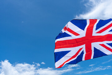 Waving UK flag under blue sky background.