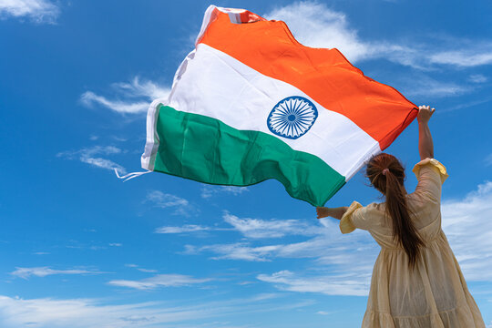 Woman Standing And Holding India Flag Under Blue Sky.