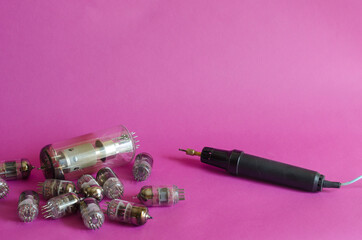 Group of random radio tubes and induction soldering iron on a pink background.