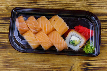 Sushi rolls Philadelphia in plastic box on wooden table. Top view. Sushi for take away or delivery of sushi in plastic container