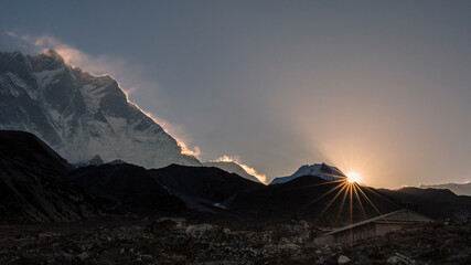 The sun rises over a mountain valley in the Himalayas, illuminating the edge of a huge snow-capped mountain