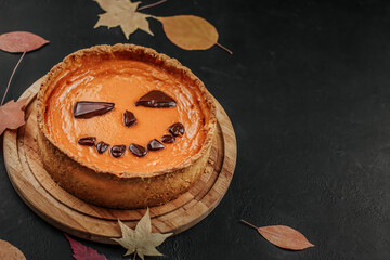 American pumpkin pie, decorated with chocolate on a black background copy space. Dry autumn leaves.