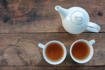 Two cups of tea and a teapot on wooden table from above. 