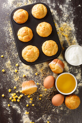 Delicious snack corn muffins in a baking dish and ingredients close-up on the table. vertical top view from above
