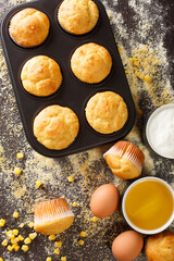 Freshly baked corn muffins in a baking dish and ingredients close-up on the table. vertical top view from above