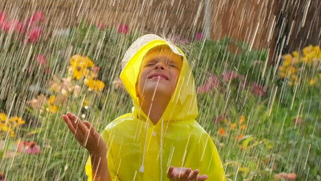 Little happy cute boy child wearing yellow raincoat and enjoying having fun rainfall. Kid playing with the rain in the sunlight. Happy family summer autumn fall childhood dream concept. 120 slow-mo