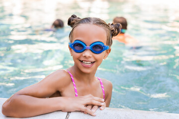 girl in swim goggles looking at camera at poolside
