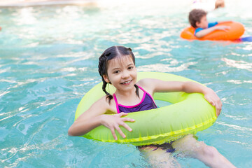 joyful girl looking at camera while floating in pool on swim ring
