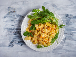 Curly pasta with vegetables, basil and arugula on a white plate on a black and white napkin top view