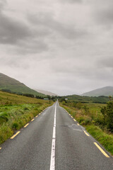Small narrow road without hard shoulder in Connemara, Ireland, Mountains covered with low cloudy sky. Nobody.