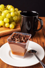 Finest chocolate dessert with chocolate chunks in focus, black cup with tea and fresh green grapes out of focus, Black background.