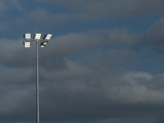 Powerful LED light on a metal pole turned on, cloudy sky background. Concept sport event, game.