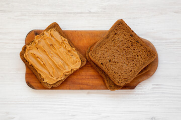 Bread Slices with Peanut Butter on a rustic wooden board on a white wooden background, top view. Flat lay, overhead, from above.