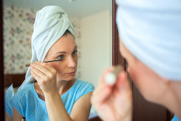 A girl with a towel on her head paints her eyelashes with mascara. The woman is going to work....