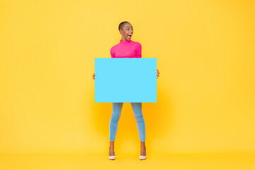 Excited pretty African American woman holding blue paper board with empty space for text on yellow...