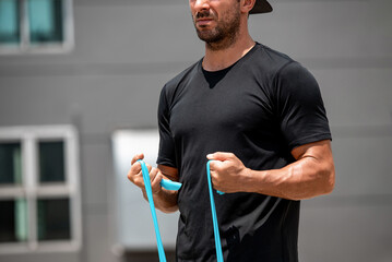 Fit muscular sports man doing bicep curl exercise with resistance band at home in the open air