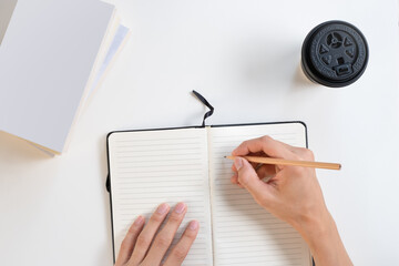 Top view of hand writing something on notebook with a cup of coffee and books on white background