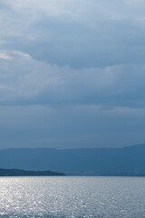 Evening view of Swiss side of Geneva Lake from French shore. Beautiful cloudscape and sun light glow on the calm water.