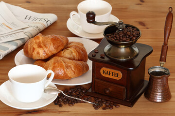 coffee still life - old coffee grinder, coffee cup, croissant, beans, cezve and german newspaper