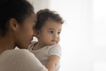Close up head shot loving young african ethnicity woman holding embracing cute sweet infant child,...