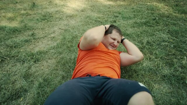 fat man engaged in fitness outdoors doing exercise for abdominal press lying on the grass