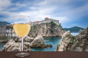Glass of white wine against Dubrovnik background. Vacation concept. Beach and city wall in historic center of Dubrovnik, Croatia
