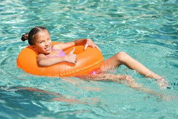 girl showing thumb up while swimming in pool on inflatable ring