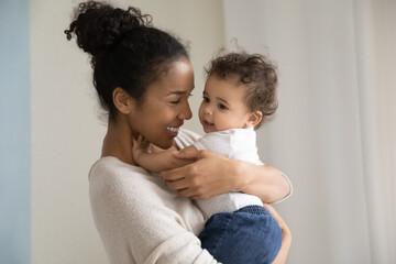 Head shot affectionate millennial biracial mommy or babysitter carrying on hands funny cute curly...
