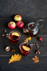 Obraz na płótnie Canvas Two cups of autumn warming tea with berries and pieces of apples on a black wooden background. Hot berry tea.