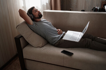 Man on sofa with headphones and notebook at home