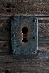 Rusted antique keyhole on a wooden doorframe.