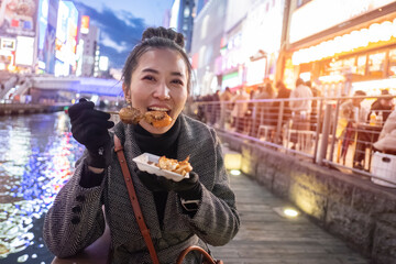 Young woman tourists enjoy eating street food in walking at street shopping center Dotonbori in Osaka, Japan.