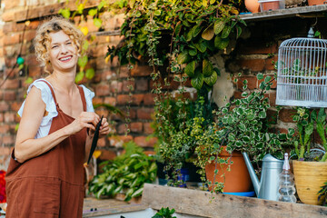 Gardener in overalls working, cleaning, taking care of plants in cozy yard or terrace at open air....