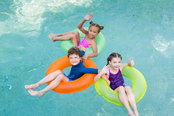 high angle view of joyful friends waving hands and looking at camera while floating in pool on swim rings