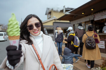 Young tourist woman eating ice cream cone street food at bamboo forest Arashiyama in Japan