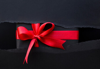 gift with a red ribbon inside a black torn paper. black Friday