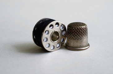 Sewing supplies. Thimble and bobbin with black threads on a gray background
